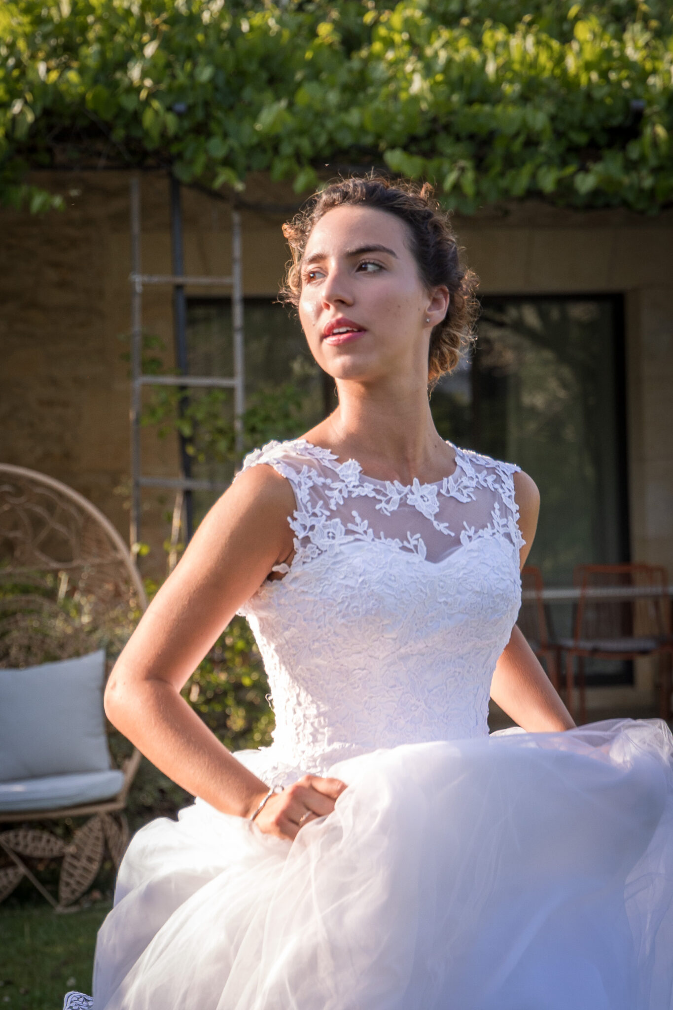 Portrait d’une mariée élégante en robe blanche, regardant au loin, baignée de lumière naturelle.