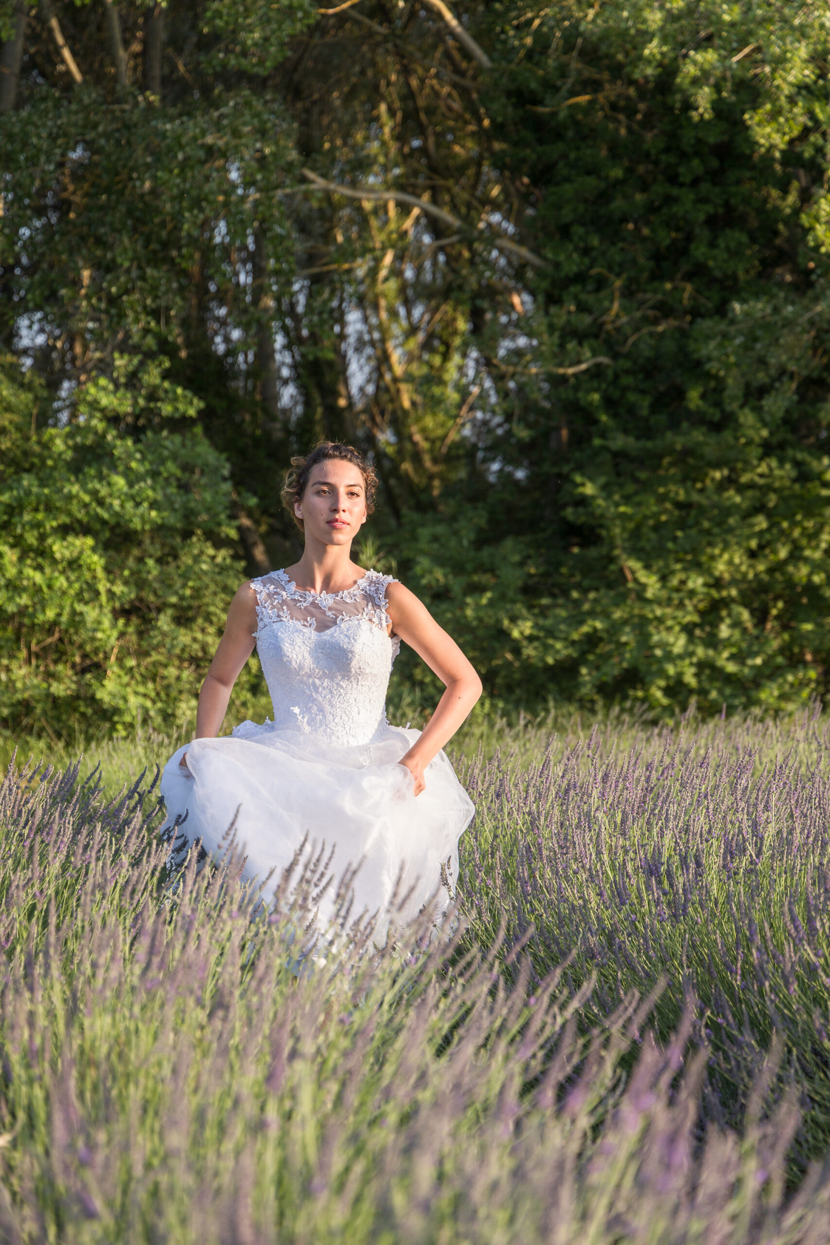 Mariée en robe blanche, debout dans un champ de lavande ensoleillé.