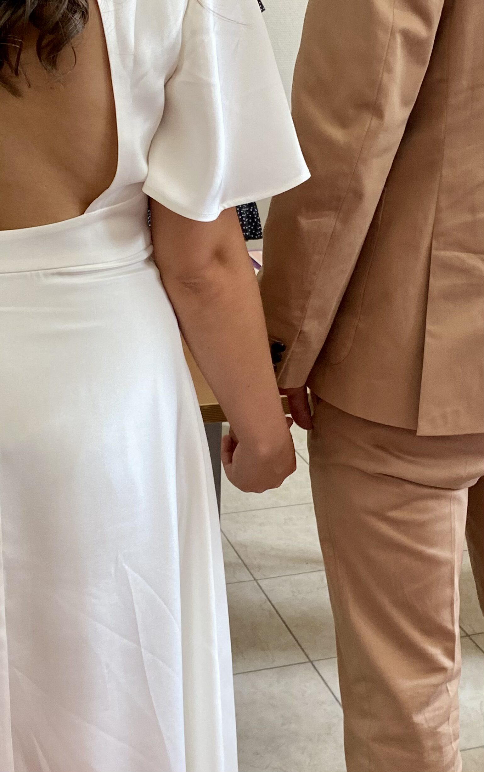 Un couple de jeunes mariés se tient la main, photographié de dos après leur cérémonie civile.