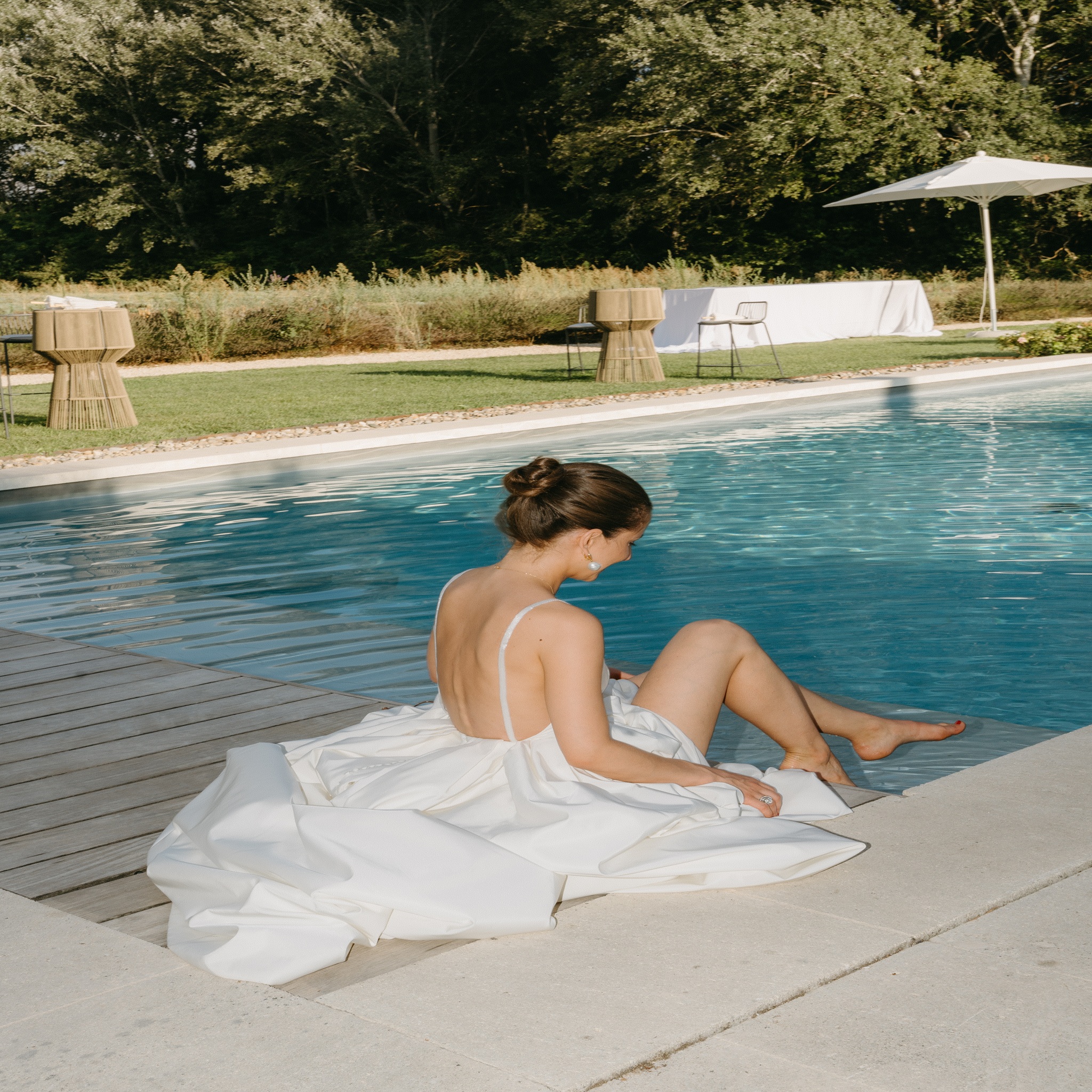 Mariée assise au bord d’une piscine dans sa robe blanche, moment de détente lors d’un mariage en Provence – L’effet Maria wedding planner