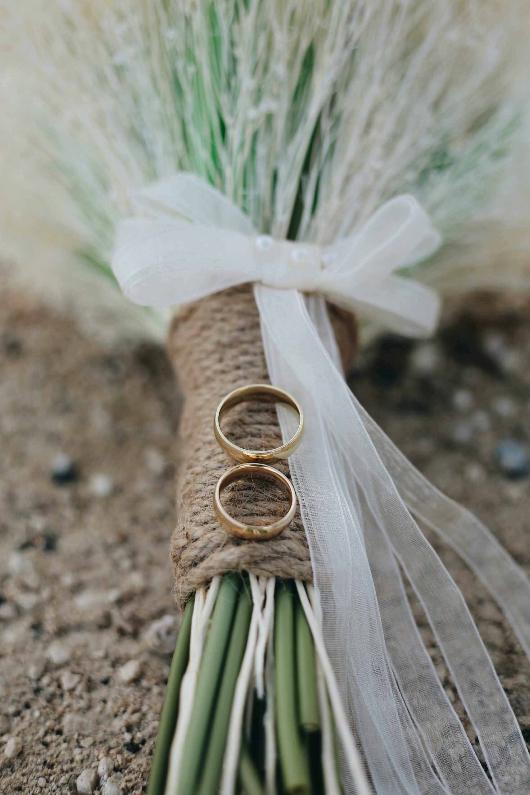 Deux alliances posées sur un bouquet rustique de graminées, décoré d’un ruban blanc.