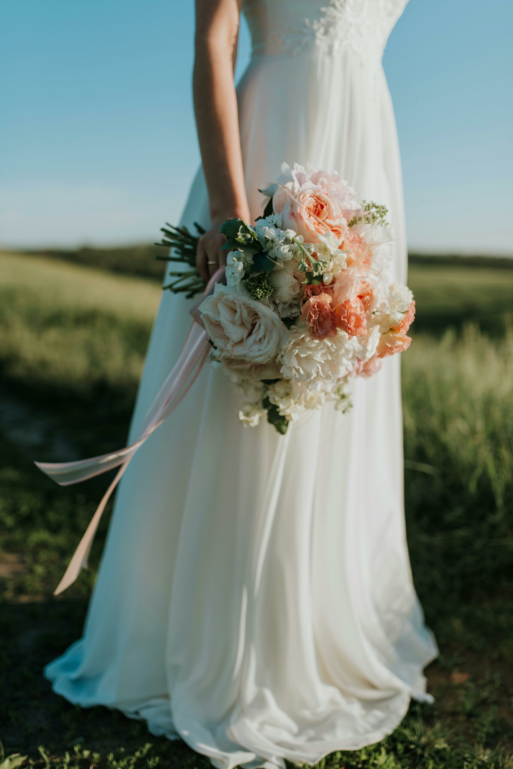 Main d’une mariée tenant un bouquet de fleurs aux tons pêche et blanc – instant élégant capturé lors d’un mariage organisé par L’effet Maria