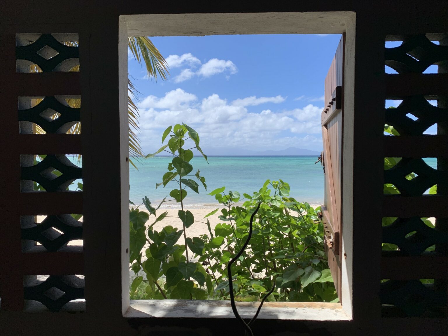 Vue sur la mer des Caraïbes à travers une fenêtre encadrée de volets en bois, en Guadeloupe by l'effet maria